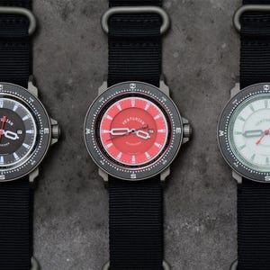 May include: Three wristwatches with black nylon straps. The watch faces are dark grey, red, and white, each with a different colour scheme and the brand name "Venturian". The watches have a compass-style bezel.