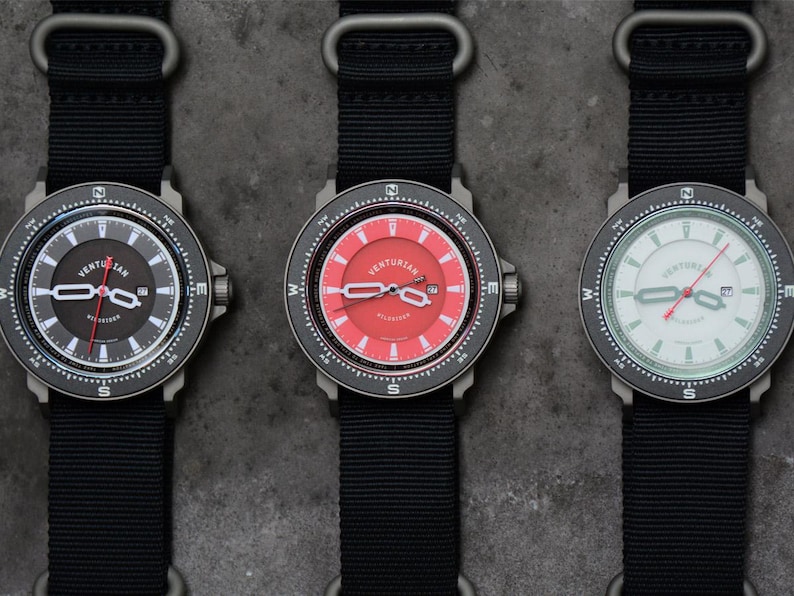 May include: Three wristwatches with black nylon straps. The watch faces are dark grey, red, and white, each with a different colour scheme and the brand name "Venturian". The watches have a compass-style bezel.