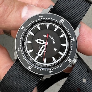 May include: Black wristwatch with a black dial and a black nylon strap. The watch face features white numerals, hands, and text, including "Veturian." The watch has a compass-style bezel and a red second hand. The watch is designed for exploration.