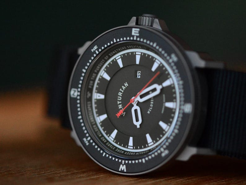 May include: Black wristwatch with a black face, white markers, and a red second hand. The watch has a black bezel with white markings and the text "VENTURIAN" on the face. The watch band is black.