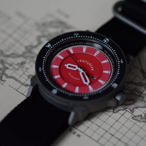 May include: A black and red VENTURIAN wristwatch with a black nylon strap. The watch face is red with white markings and hands. The watch is set against a vintage map background. The watch has the text "UNDER MORE STARS AND WILDER LANDSCAPES".
