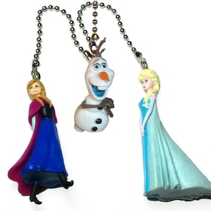 May include: Three fan pull chains featuring characters from the film Frozen. The characters include Anna in a blue and purple dress, Olaf the snowman, and Elsa in a blue and light blue dress. Each character is attached to a silver ball chain.