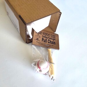 Pu&ograve; includere: Una catenella per ventilatore a soffitto e luce con una mazza da baseball in legno in miniatura e una pallina da baseball con cuciture rosse. L'articolo &egrave; confezionato in un sacchetto di plastica trasparente con un'etichetta in cartone.