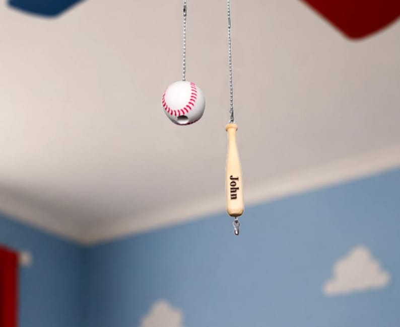 Pu&ograve; includere: Due catenelle per ventilatore a soffitto con una pallina da baseball bianca con cuciture rosse e una mazza da baseball in legno chiaro. La mazza presenta il nome John inciso in lettere nere sul lato. Entrambi pendono da catenelle metalliche.