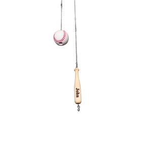 Pu&ograve; includere: Una catenella per ventilatore a soffitto con una pallina da baseball bianca con cuciture rosse e una mazza da baseball in legno chiaro. La mazza presenta il nome John inciso in caratteri scuri. Entrambi gli oggetti sono fissati a catenelle metalliche.