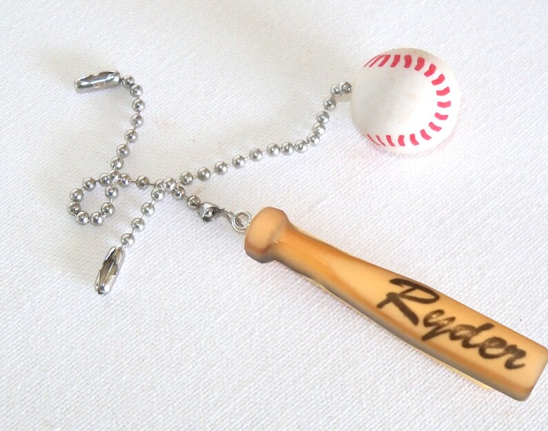 Pu&ograve; includere: Una catenella per ventilatore a soffitto con una pallina da baseball bianca con cuciture rosse e un ciondolo a forma di mazza da baseball in legno marrone chiaro. Sulla mazza &egrave; inciso il nome Ryder in corsivo scuro. Collegati da una catenella a palline.
