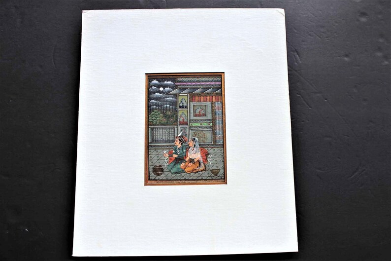 May include: A framed miniature painting depicting a couple sitting on a balcony. The painting is set against a backdrop of a building with a window and a cloudy sky. The couple is dressed in traditional Indian clothing and is holding a cup and a plate.