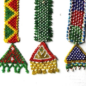 May include: Three beaded ornaments with triangular shapes and fringe. The ornaments are red, green, and blue with white accents.