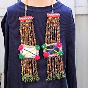 May include: Two long beaded necklaces with mirrors and colorful tassels. The necklaces are brown with red, yellow, green, and blue accents.