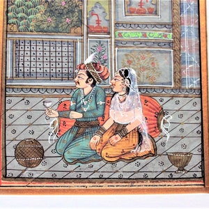 May include: A traditional Indian miniature painting depicting a couple in a palace setting. The man is wearing a blue and gold turban and holding a glass of wine. The woman is wearing a white veil and a yellow and orange dress. The painting is done in a vibrant style with intricate details.