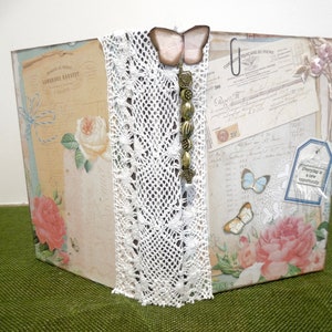 May include: A vintage-style scrapbook with a white lace trim, a butterfly charm, and a tag that reads "Everyday is a new opportunity". The scrapbook is decorated with floral patterns and old paper ephemera.