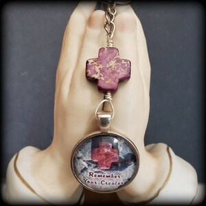May include: A silver keychain with a purple and white cross charm and a round glass charm with a purple cross and the text "Remember Your Creator".