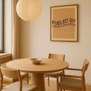 May include: A dining room with a round wooden table and four chairs. A framed poster on the wall says "Fueled by Coffee & Delusions." A paper lantern hangs from the ceiling, and a small bowl sits on the table.