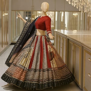 Puede incluir: Un maniquí exhibe un lehenga indio tradicional. El conjunto presenta un top corto rojo de manga larga, una falda estampada con paneles rojos, beige y marrones y un chal negro con ribete dorado. La falda tiene un dobladillo ancho con pequeños adornos.