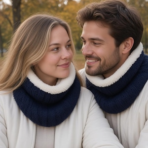 May include: Two individuals wearing matching navy blue infinity scarves with a white sherpa fleece lining. The scarves feature a textured knit exterior and a soft, plush interior, worn over cream-colored zip-up jackets in an outdoor setting.