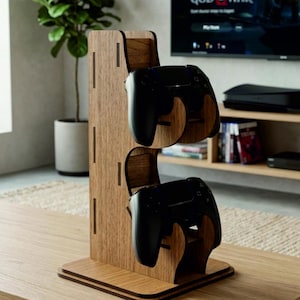 May include: A vertical wooden stand with a light brown wood grain finish designed to hold two black video game controllers. The stand features a flat rectangular base and two stacked, curved cradles that securely support the controllers.
