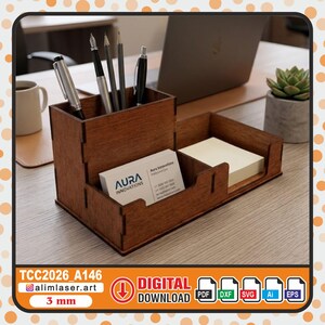 May include: A dark brown wooden desk organizer with a tall compartment for pens and pencils, and two lower sections for business cards and sticky notes. The business card features the text Aura Innovations. The organizer is made of 3 mm thick wood.
