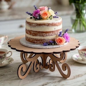 Op de afbeelding: Een naked cake met lagen witte glazuur, bekroond met roze, perzik en crèmekleurige rozen en paarse lavendeltakjes, rustend op een lichtbruine houten taartstandaard met een geschulpte rand en sierlijke, gebogen poten op een marmeren blad.