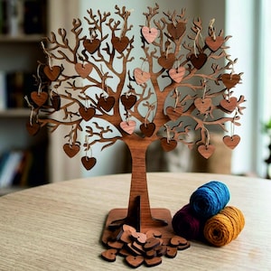 May include: A brown wooden tree-shaped display stand with multiple branches, featuring numerous small wooden heart-shaped ornaments hanging from the twigs by thin strings. A pile of loose wooden hearts sits at the base, alongside three yarn balls.