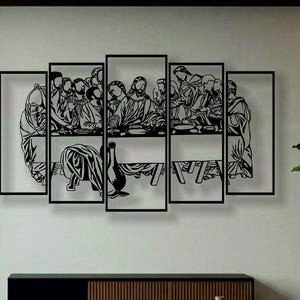 Könnte beinhalten: Ein Wandkunstobjekt aus schwarzem Metall, das das Abendmahl darstellt und aus fünf rechteckigen Paneelen unterschiedlicher Höhe besteht. Das Design zeigt eine zentrale Figur an einem langen Tisch, umgeben von zwölf Personen als Silhouette.