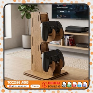 Op de afbeelding: Een lichtbruine houten standaard voor gamecontrollers met twee sleuven voor zwarte controllers. De standaard heeft een modern ontwerp. De tekst "TCC2026_A065" en "alimlaser.art" zijn zichtbaar.