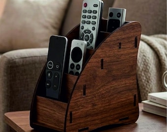 May include: A dark brown wood grain finish remote control organizer with a tiered design featuring four distinct slots. The organizer holds four different remote controls of varying sizes and colors, including black, silver, and white plastic units.