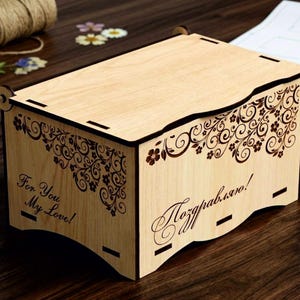 May include: A rectangular light-colored wooden box with a hinged lid. The sides feature laser-cut floral patterns and the text "For You My Love!" on one side and "Поздравляю!" on the front. The box has dark brown edges and a smooth finish.