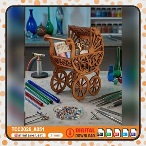 May include: A laser-cut wooden baby carriage organiser featuring intricate scrollwork patterns, four spoked wheels, and a handle. It contains sewing supplies including spools and scissors. Text includes TCC2026_A051, 3 mm, and DIGITAL DOWNLOAD.
