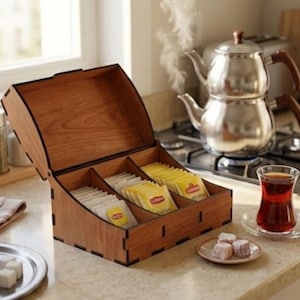 Puede incluir: Una caja organizadora de madera para bolsitas de té con la tapa abierta, que cuenta con tres compartimentos internos llenos de bolsitas de té Lipton amarillas. La caja tiene un acabado de veta de madera natural con bordes oscuros sobre una encimera.