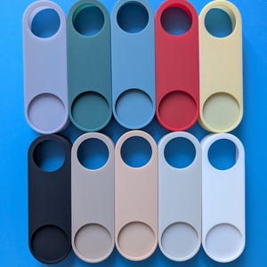 May include: A collection of ten colorful door hangers in various shades, including gray, green, blue, red, and yellow. Each hanger has a circular opening at the top and a larger circular cutout at the bottom, all against a blue background.
