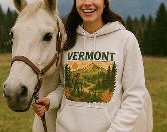Puede incluir: Sudadera blanca con la palabra "VERMONT" estampada en la parte delantera, con una escena de la naturaleza con un excursionista. La persona lleva un gorro beige y pantalones negros, de pie junto a un caballo blanco.