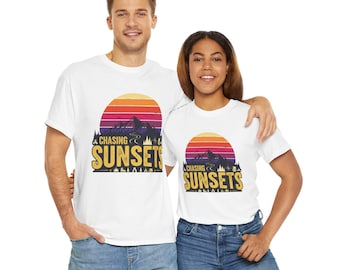May include: White t-shirts with a sunset graphic. The design features a colorful sunset over mountains with the text "Chasing Sunsets" in a stylized font. The shirts are worn by two people.