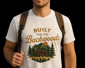 Puede incluir: Camiseta blanca con un diseño gráfico de un oso, montañas y árboles, con el texto "BUILT FOR THE Backwoods". La camiseta la lleva una persona con una mochila, sobre un fondo oscuro.