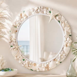 Peut inclure: Un miroir mural rond doté d'un cadre densément décoré de divers coquillages blancs et crème, de petites étoiles de mer et de morceaux de verre marin vert éparpillés. Le miroir présente une surface réfléchissante circulaire et un bord blanc.