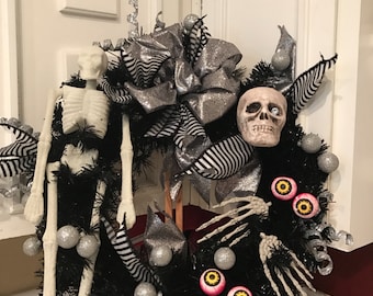 May include: A Halloween wreath with a black base, adorned with a white skeleton, skull, and eyeballs. The wreath features silver glitter accents, striped ribbons, and silver ornaments. A spooky and festive decoration.