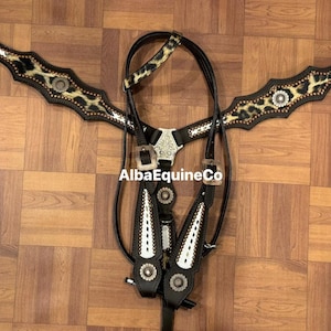 May include: Black and tan horse tack set with a leopard print design. The set includes a breast collar, headstall, and reins. The breast collar and headstall feature silver-tone hardware and decorative accents. The text "AlbaEquineCo" is visible.