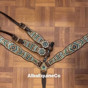 May include: A brown leather horse breast collar and headstall set. The set is adorned with turquoise, gold, and clear crystal-like embellishments. The design includes geometric patterns and floral accents.