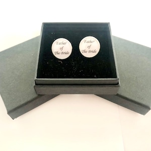 May include: A black gift box with a black velvet interior. The box contains two silver cufflinks with the inscription "Father of the Bride".