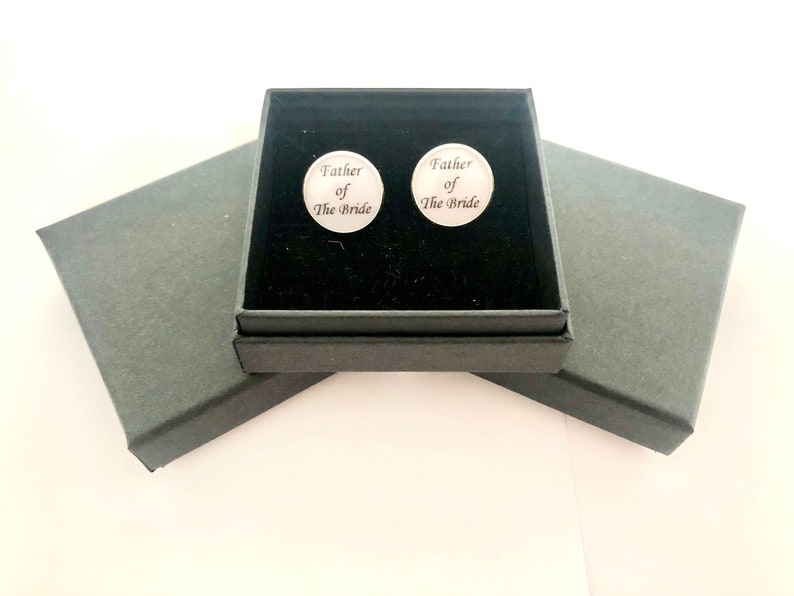 May include: A black gift box with a black velvet interior. The box contains two silver cufflinks with the inscription "Father of the Bride".