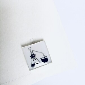 May include: A pair of cufflinks with a black and white illustration of a laboratory flask and beaker.