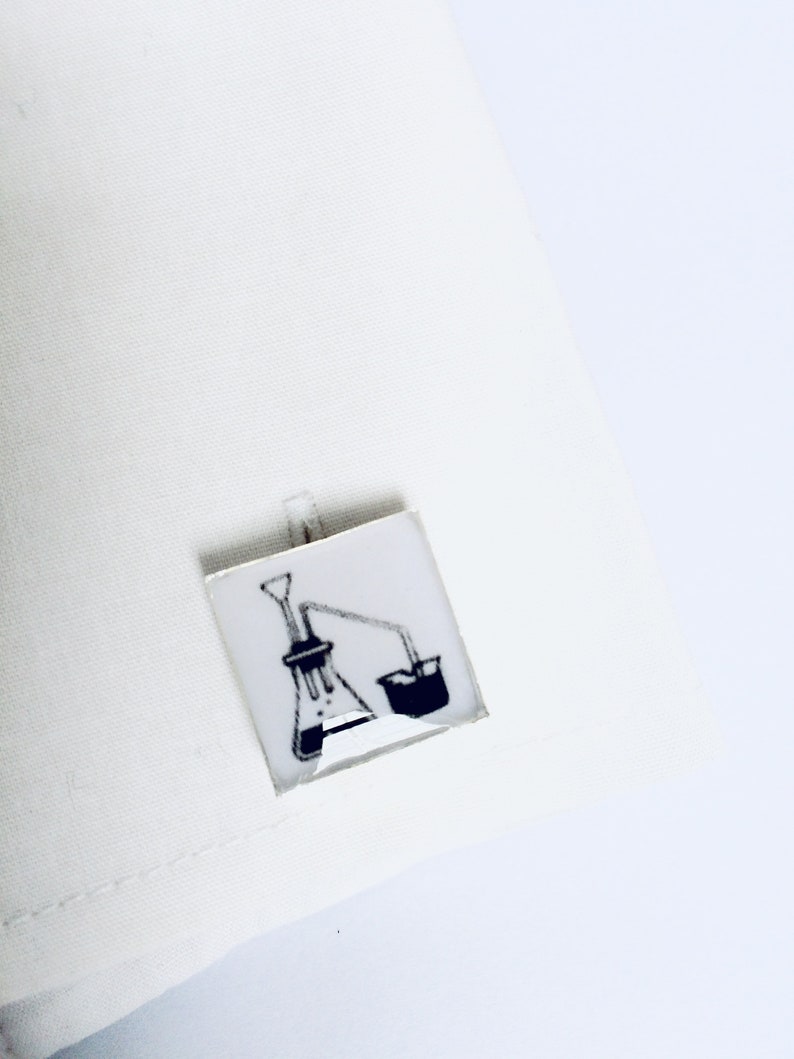 May include: A pair of cufflinks with a black and white illustration of a laboratory flask and beaker.