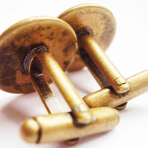 May include: A pair of gold-toned cufflinks with a smooth, rounded surface. The cufflinks are connected by a hinged bar.