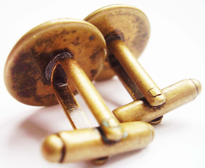 May include: A pair of gold-toned cufflinks with a smooth, rounded surface. The cufflinks are connected by a hinged bar.