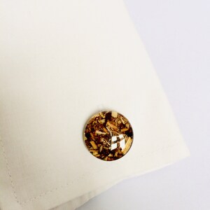 May include: A pair of cufflinks with a round, clear resin design. The resin contains small pieces of wood, creating a unique and natural look.