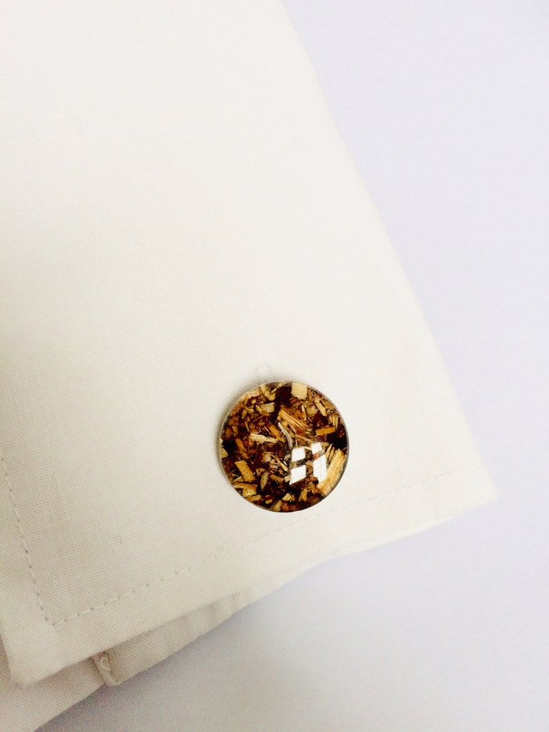 May include: A pair of cufflinks with a round, clear resin design. The resin contains small pieces of wood, creating a unique and natural look.