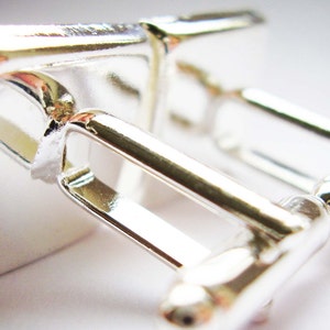 May include: A pair of silver cufflinks with a square design. The cufflinks are made of polished metal and have a simple, elegant look.