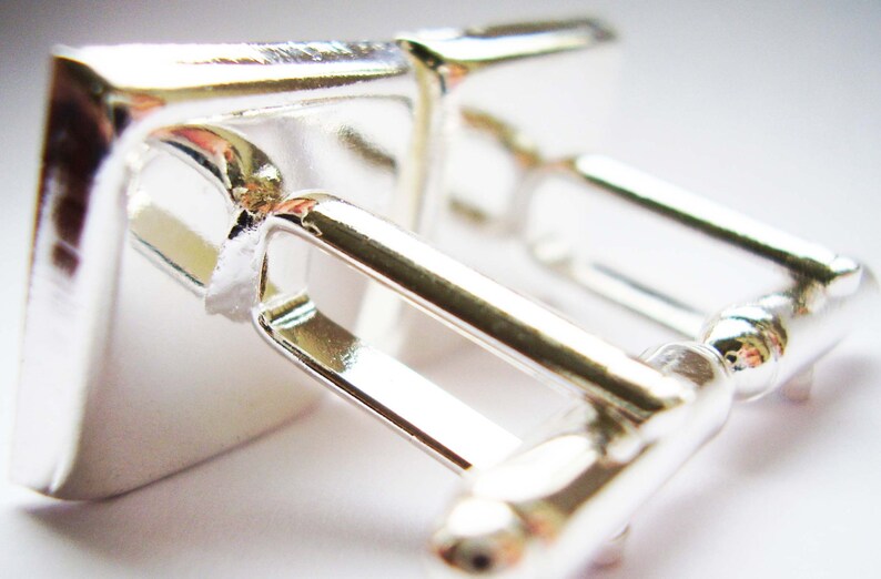 May include: A pair of silver cufflinks with a square design. The cufflinks are made of polished metal and have a simple, elegant look.