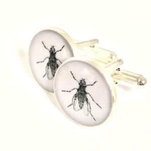 May include: A pair of silver cufflinks with a white background and a black and white image of a fly on each cufflink.