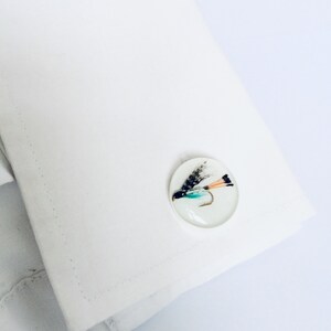 May include: A pair of cufflinks featuring a realistic fly with black, white, orange, and green feathers, encased in a clear resin oval.