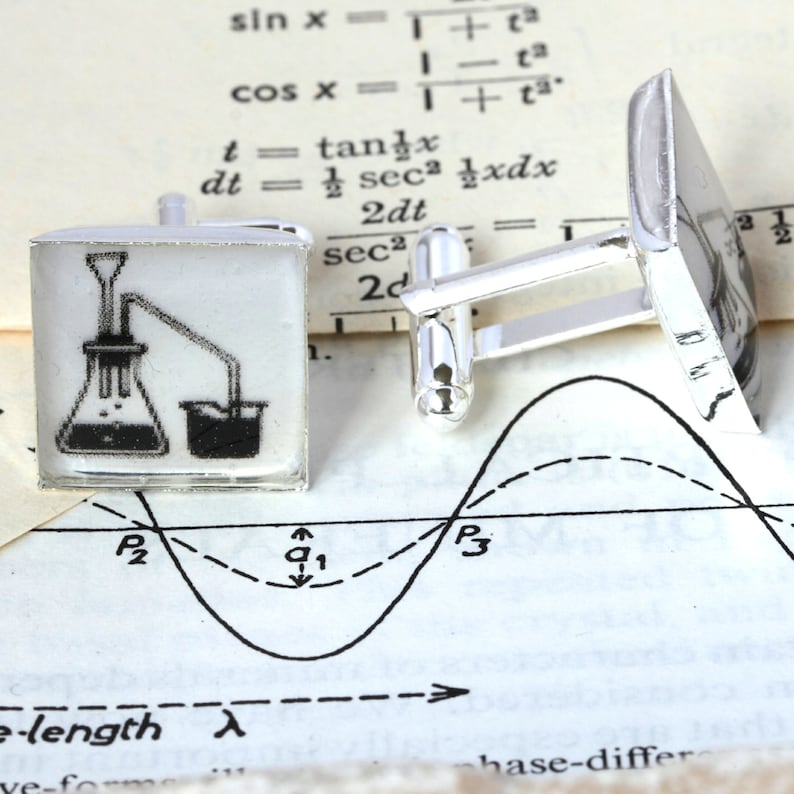 May include: A pair of silver cufflinks with a white background and a black and white illustration of a chemistry experiment. The experiment shows a flask with a tube leading to a beaker.